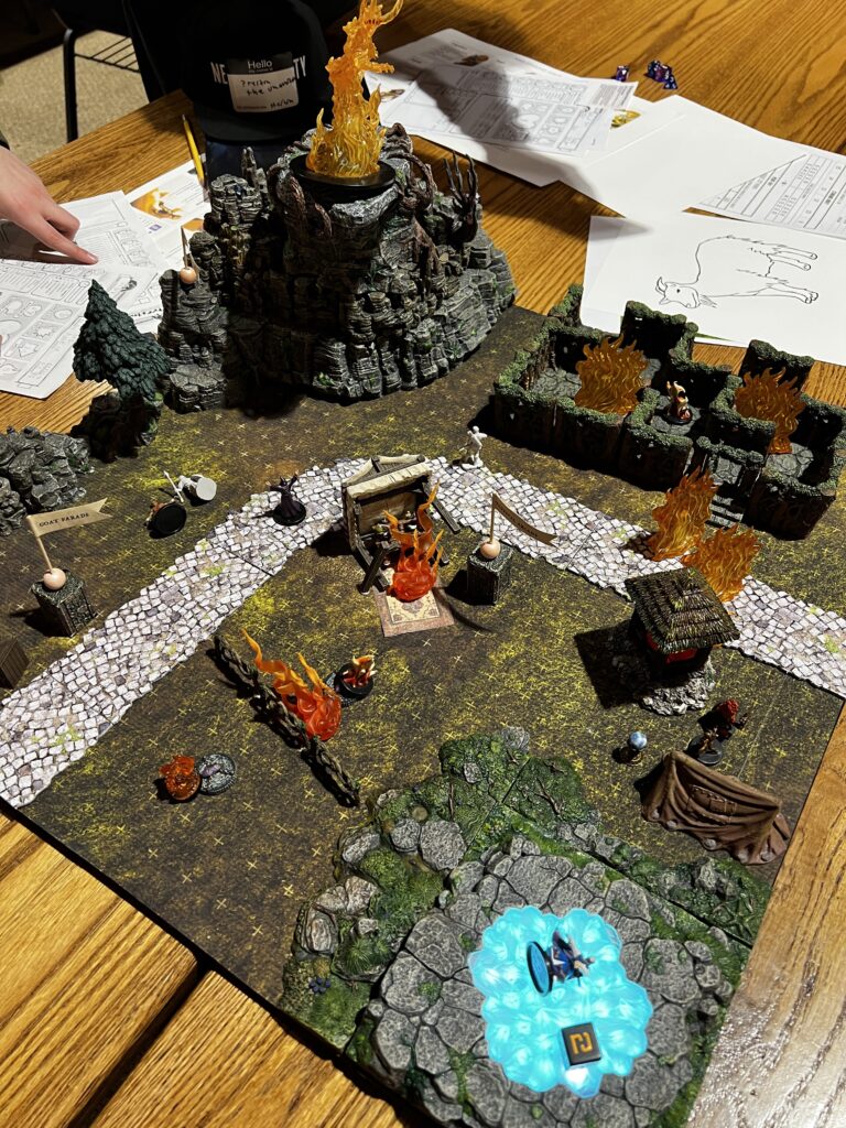 A section of the fairgrounds map with a large figurine of a fire elemental on a cliff towering above the various attractions now dotted with representations of flames by the glowing portal.